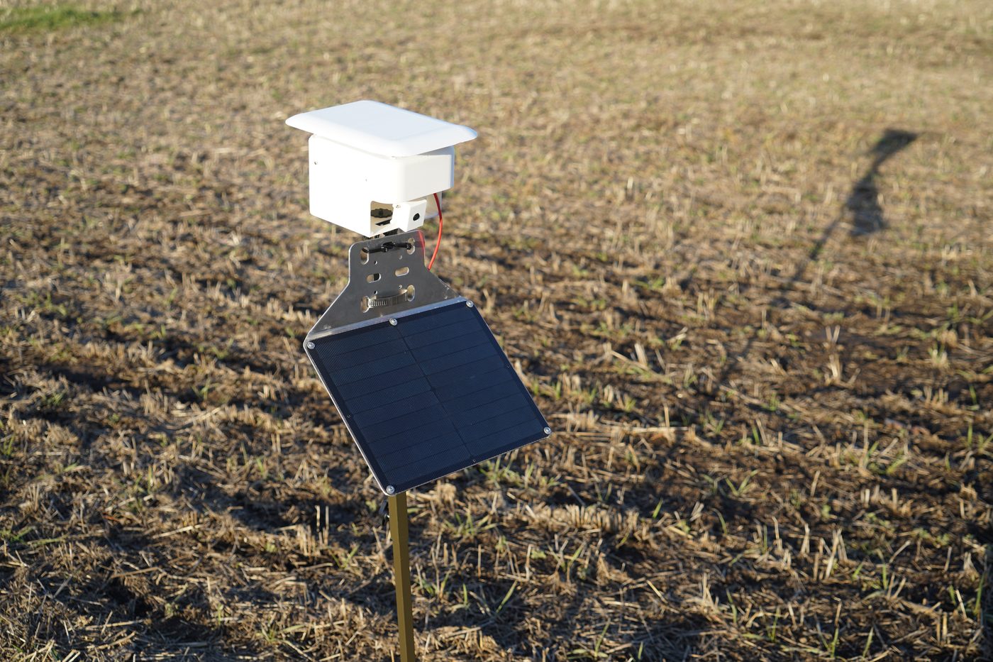 Finished unit with white enclosure, roof, and solar panel on a pole in a field
