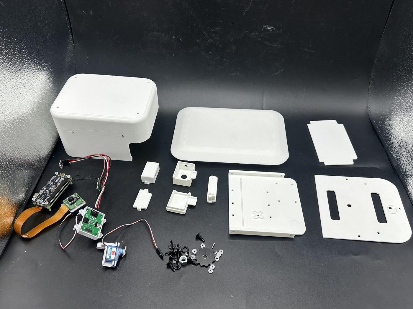 All FarmGazer enclosure parts laid out: white 3D-printed main body, roof, plates and small housings, with the Raspberry Pi, camera, servos and cables