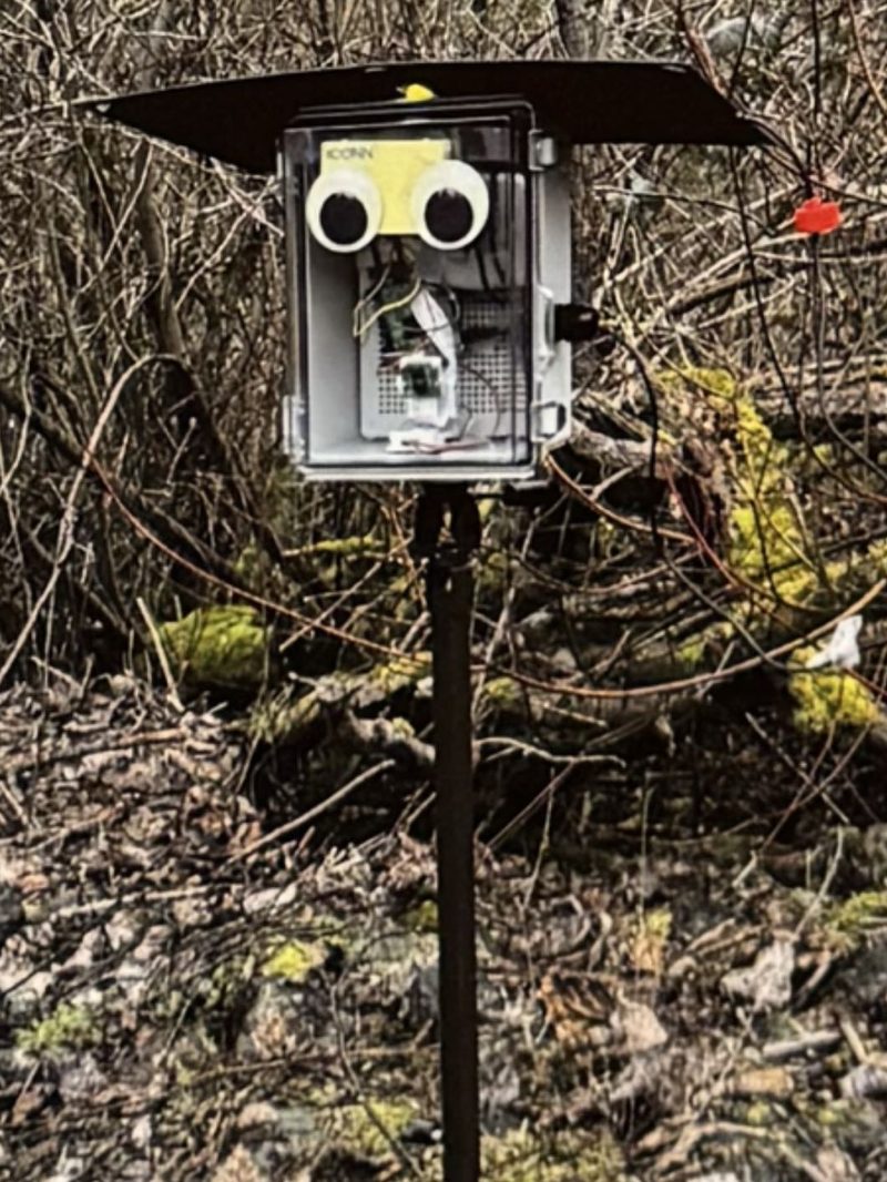 FarmGazer 1.0: a clear plastic junction box with the camera behind its cover, under a flat sheet roof